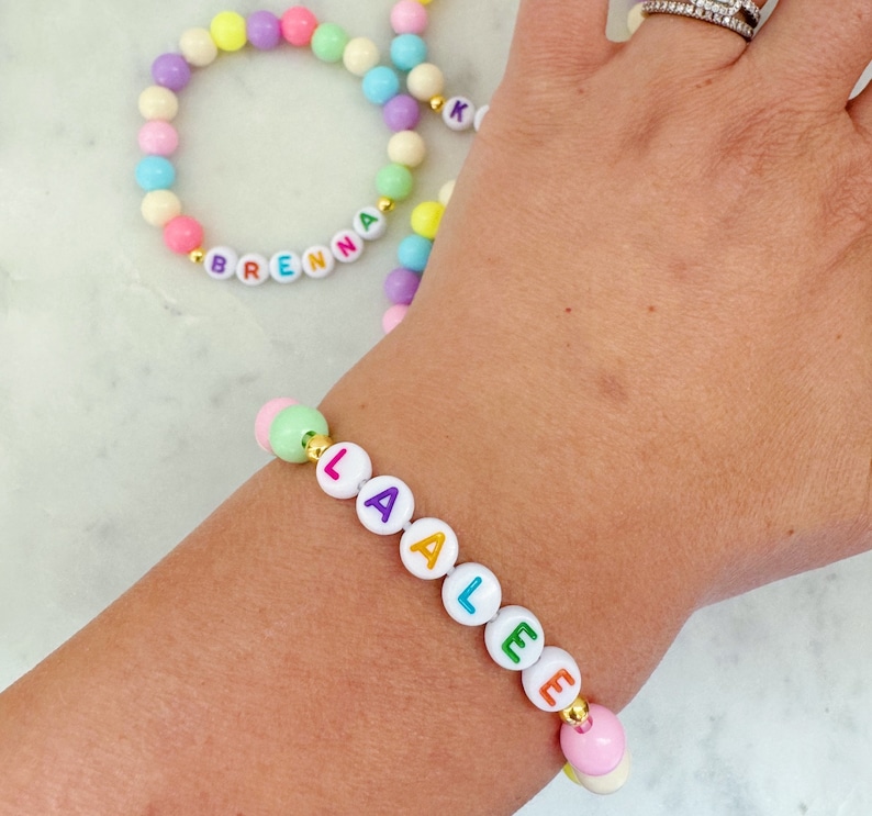 May include: Two colorful beaded bracelets with the names "Brenna" and "Laalee" spelled out in colorful letters. The bracelets are made with white beads and colorful letters.