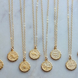 May include: Twelve gold necklaces with zodiac signs as pendants. The signs are: Libra, Scorpio, Sagittarius, Capricorn, Aquarius, Pisces, Aries, Taurus, Gemini, Cancer, Leo, and Virgo.