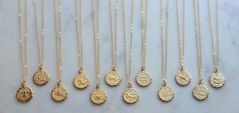 May include: Twelve gold necklaces with zodiac signs as pendants. The signs are: Libra, Scorpio, Sagittarius, Capricorn, Aquarius, Pisces, Aries, Taurus, Gemini, Cancer, Leo, and Virgo.