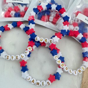 May include: Four red, white, and blue star-shaped bead bracelets with gold letters spelling out the names "Stella", "Luke", "James", and "Caroline".