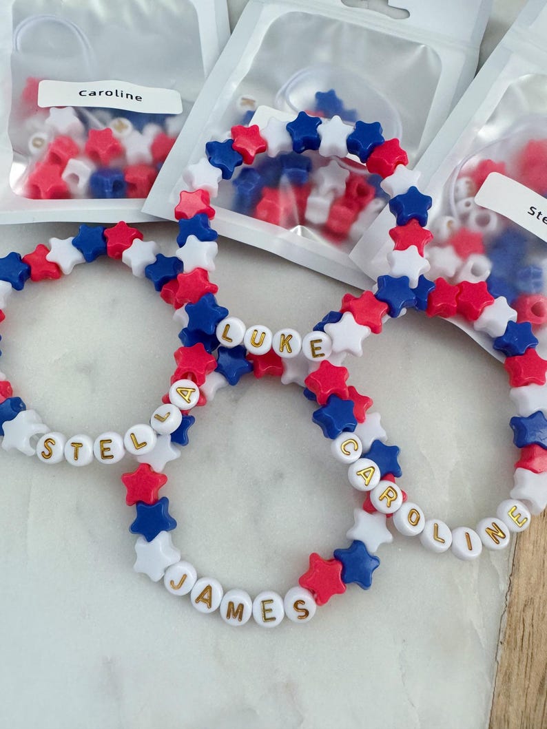 May include: Four red, white, and blue star-shaped bead bracelets with gold letters spelling out the names "Stella", "Luke", "James", and "Caroline".