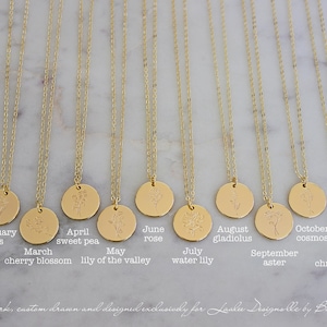 Peut inclure: Colliers dor&eacute;s avec des pendentifs ronds grav&eacute;s chacun d'une fleur et d'un mois diff&eacute;rents. Les mois sont de janvier &agrave; d&eacute;cembre, avec les noms des fleurs correspondantes en dessous. Le texte "original artwork, custom drawn and designed exclusively for Laalu Designe by Badu Landes" est en bas.
