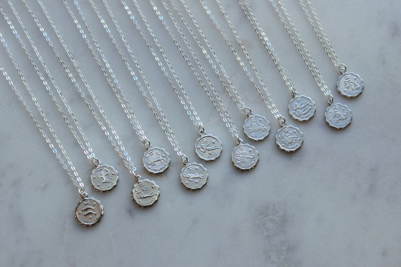 Puede incluir: Un conjunto de doce collares de plata con colgantes de signos del zod&iacute;aco. Cada collar presenta una delicada cadena de plata y un peque&ntilde;o colgante redondo con un s&iacute;mbolo del zod&iacute;aco.
