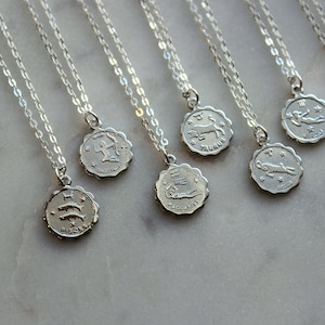 Puede incluir: Un conjunto de collares de plata con colgantes de signos del zod&iacute;aco. Cada colgante presenta un s&iacute;mbolo del zod&iacute;aco diferente, incluidos Piscis, Acuario, Tauro, Sagitario, Virgo, Escorpio y Capricornio.