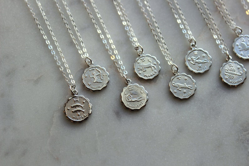Puede incluir: Un conjunto de collares de plata con colgantes de signos del zod&iacute;aco. Cada colgante presenta un s&iacute;mbolo del zod&iacute;aco diferente, incluidos Piscis, Acuario, Tauro, Sagitario, Virgo, Escorpio y Capricornio.