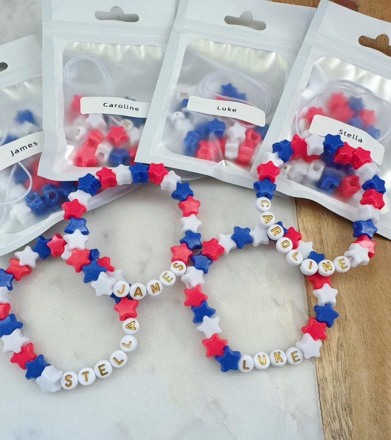 May include: Four red, white, and blue star-shaped bead bracelets with gold lettering spelling out the names "James", "Stella", "Caroline", and "Luke".