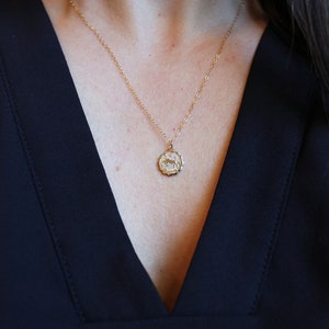 May include: A gold chain necklace with a small, round pendant featuring a zodiac symbol. The pendant has a textured, ornate design.