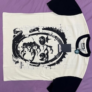 Könnte beinhalten: Cremefarbenes T-Shirt mit schwarzen Ärmeln und Kragen. Das Shirt hat einen großen, schwarzen, abgenutzten Aufdruck auf der Vorderseite mit dem Text "HELLSTAR". Ein Etikett mit dem Markennamen ist angebracht.