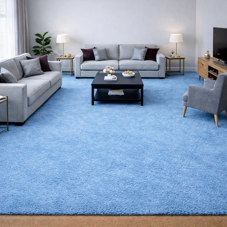 May include: A living room with light blue carpet, two gray sofas, and a black coffee table. The room is furnished with a wooden cabinet, two side tables with lamps, and a gray armchair. Decorative pillows and plants add color.