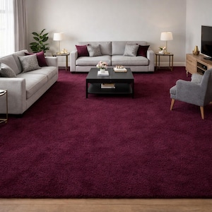 May include: A living room featuring a large, plush, burgundy area rug. Two light gray sofas with accent pillows sit on the rug, along with a black coffee table and a gray armchair. Two side tables with lamps and a TV cabinet complete the room.