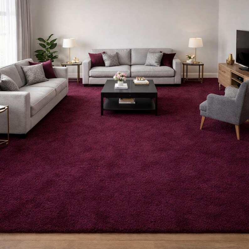 May include: A living room featuring a large, plush, burgundy area rug. Two light gray sofas with accent pillows sit on the rug, along with a black coffee table and a gray armchair. Two side tables with lamps and a TV cabinet complete the room.