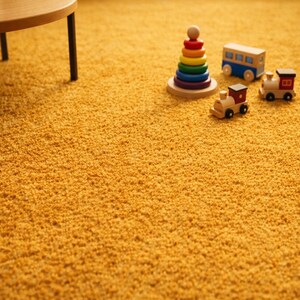 May include: A close-up shot of a golden-yellow shag carpet with a wooden table leg in the upper left corner. A wooden toy train, bus, and a rainbow-colored stacking toy are on the carpet.