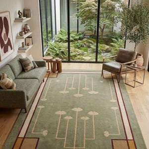 Könnte beinhalten: Wohnzimmer mit einem grünen Teppich mit geometrischem Design. Der Teppich hat einen hellgrünen Hintergrund mit cremefarbenen und burgunderfarbenen Akzenten. Ein grünes Sofa, ein Sessel und Beistelltische aus Holz sind ebenfalls im Raum. Ein großes Fenster blickt auf einen Garten.
