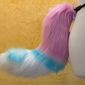 A luxury faux fur wild dog themed fursuit tail.

The base of the tail is Candy pink, tip is white. A white with turquoise tipped fabric band separates the two colours. There is also a white with turquoise tipped fabric spot on the top of the white section. 

Great fur cosplays and costumes