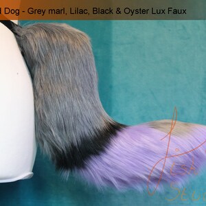 A luxury faux fur wild dog themed fursuit tail.

The base of the tail is grey, tip is lilac. A black band seperates the two colours. There is also an oyster colour spot on the top of the lilac section. 

Great fur cosplays and costumes