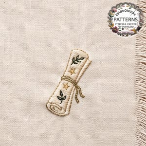 May include: An embroidered design on cream-colored fabric featuring a rolled parchment scroll tied with a string. The scroll is decorated with two gold-colored stars and two dark green leafy sprigs. The embroidery uses satin and back stitches.