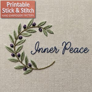 Pode incluir: Design bordado em tecido bege com um ramo de oliveira verde com azeitonas roxas e as palavras "Inner Peace" em azul marinho. Um pequeno retângulo laranja no canto superior esquerdo diz "Printable Stick & Stitch Hand Embroidery Pattern."