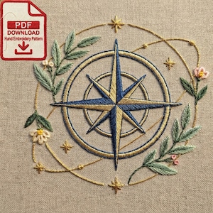 May include: Hand embroidery pattern featuring a compass rose design in blue and gold, surrounded by floral and leaf accents. The design is on a beige fabric. The image includes the text "PDF DOWNLOAD Hand Embroidery Pattern".