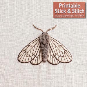 May include: An embroidery design of a moth with a fuzzy grey body and cream-colored wings featuring dark brown vein details. The design includes two thin antennae and is accompanied by a rectangular label with the text Printable Stick & Stitch.
