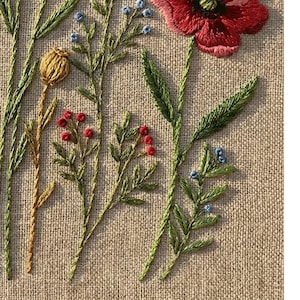 Peut inclure: Gros plan d'une broderie florale sur un fond de tissu beige. La broderie pr&eacute;sente un grand coquelicot rouge, des feuilles vertes et des tiges avec de petites baies rouges et bleues. Les points cr&eacute;ent un aspect textur&eacute; et artisanal.