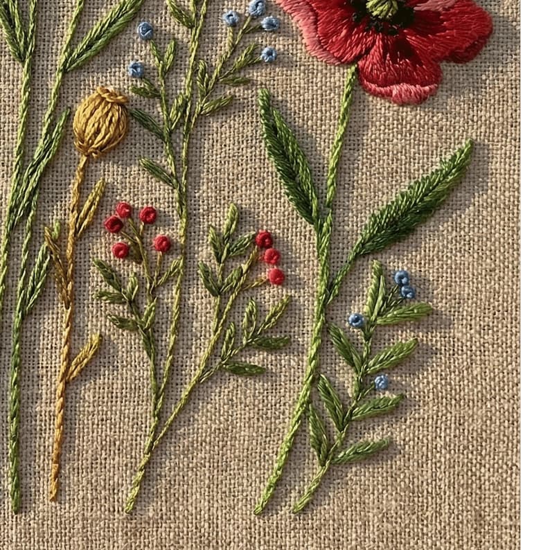 Peut inclure: Gros plan d'une broderie florale sur un fond de tissu beige. La broderie pr&eacute;sente un grand coquelicot rouge, des feuilles vertes et des tiges avec de petites baies rouges et bleues. Les points cr&eacute;ent un aspect textur&eacute; et artisanal.