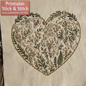 May include: Embroidered heart-shaped design featuring a world map filled with floral and botanical elements. The design is outlined in gold thread and set against a beige fabric. The text "Printable Stick & Stitch Hand Embroidery Pattern" is in the upper left corner.