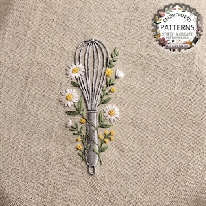 May include: An embroidery design on beige fabric featuring a silver wire whisk surrounded by white daisies with yellow centres and small yellow floral sprigs with green leaves. A circular logo in the corner reads EMBROIDERY PATTERNS STITCH & CREATE.