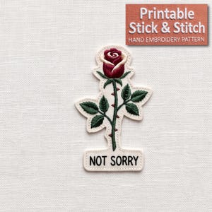 May include: An embroidered patch featuring a deep red rose with green leaves and a thorny stem on a cream-colored background. Below the rose, a rectangular tab contains the black text NOT SORRY. The design is outlined in a cream border.