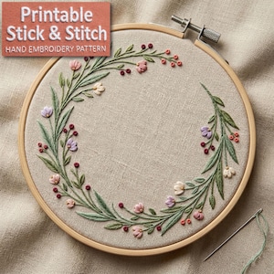 Può includere: Un modello di ricamo a mano in un telaio di legno. Il design presenta una ghirlanda floreale con fiori rosa, viola e bianchi, foglie verdi e bacche rosse. Il testo "Printable Stick & Stitch Hand Embroidery Pattern" è in alto a sinistra.