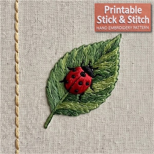 Può includere: Un disegno da ricamo su tessuto beige chiaro raffigurante una coccinella rossa con punti neri su una foglia verde. Una linea verticale di cuciture gialle corre lungo il lato sinistro. Il testo in alto a destra recita: Printable Stick & Stitch HAND EMBROIDERY PATTERN.