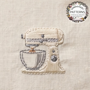 Puede incluir: Un diseño de bordado sobre tela beige que muestra una batidora de pie en hilo crema y gris. La batidora tiene un tazón y un batidor. Un logotipo circular en la esquina superior derecha dice EMBROIDERY PATTERNS STITCH & CREATE PDF DOWNLOAD.
