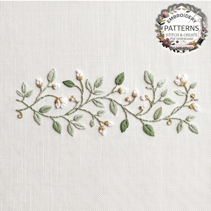 Könnte beinhalten: Ein Stickmuster mit einer horizontalen Ranke aus salbeigrünen Blättern und kleinen weißen Blüten mit gelben Mitten auf weißem Stoff. Ein kreisförmiges Logo oben rechts trägt die Aufschrift EMBROIDERY PATTERNS STITCH & CREATE.