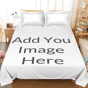 May include: White bedsheet set with two white pillowcases. The bedsheet has the text "Add You Image Here" in large, dark gray letters. The bed is made up and ready for use.