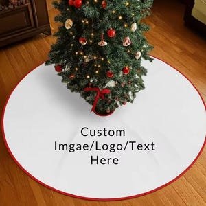 以下が含まれることがあります： 赤い縁取りが施された円形の白いクリスマスツリースカート。中央には黒い文字で「Custom Imgae/Logo/Text Here」とプリントされており、赤いオーナメントと温かみのある白いイルミネーションで飾られたクリスマスツリーの下に敷かれています。