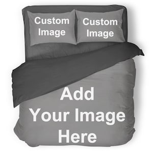 Peut inclure: Une parure de lit grise et noire comprenant deux taies d'oreiller et une housse de couette. Les taies d'oreiller affichent le texte "Custom Image", et la housse de couette le texte "Add Your Image Here" en blanc. L'ensemble est présenté sur un lit.