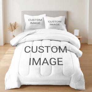 May include: A white bed set featuring a comforter and two pillowcases. The comforter and pillowcases have the text "CUSTOM IMAGE" printed on them. The bed set is on a bed with a light grey headboard.