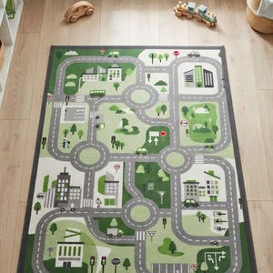 May include: A rectangular area rug featuring a printed city map design with gray roads, green park areas, and various buildings. The graphic includes traffic lights, road signs, and small vehicles set against a light green and white background.