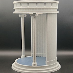 May include: A 3D-printed model of a classical structure with a circular base and top. The model features two columns, a blue interior floor, and detailed architectural elements. The structure is a light grey colour.