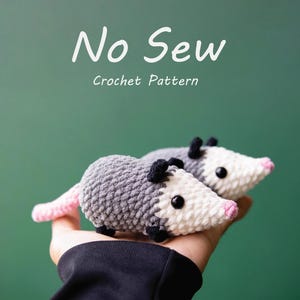 Può includere: Due opossum all'uncinetto con corpi grigi, facce bianche e nasi e code rosa. Gli opossum hanno occhi e orecchie neri. Il testo "No Sew Crochet Pattern" è in scrittura bianca sopra gli opossum.