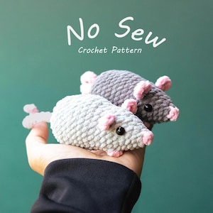 Puede incluir: Dos ratones de crochet, uno gris claro y otro gris oscuro, con orejas y narices rosas. Los juguetes se sostienen en una mano sobre un fondo verde azulado. El texto "No Sew Crochet Pattern" está en la parte superior.