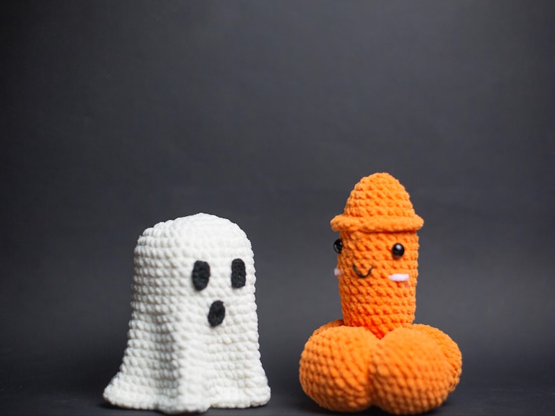 May include: Two handmade crochet figures against a dark backdrop. One is a white ghost with black eyes and mouth. The other is an orange figure with a hat, eyes, and a smiling face. Halloween-themed decorations.