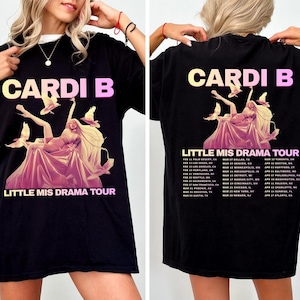 May include: Black t-shirt featuring a graphic of a woman in a flowing gown with birds, the text "CARDI B" in yellow and pink, and "LITTLE MIS DRAMA TOUR". The back of the shirt includes tour dates.