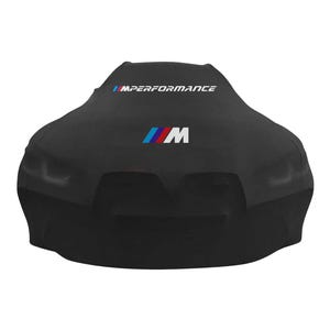 Puede incluir: Una funda de coche negra con el texto "IMPERFORMANCE" en blanco y azul. La funda también presenta el logotipo "M" en azul, rojo y blanco. La funda está diseñada para adaptarse a un coche.