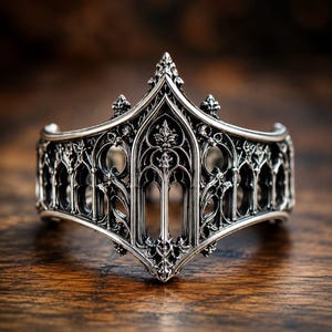 Peut inclure: Un bracelet manchette en argent présentant un design ajouré complexe inspiré par des arches architecturales et des fenêtres en ogive. Le métal possède une finition polie avec des zones en creux assombries soulignant les motifs filigranés.