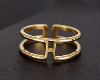 Anello a doppia fascia in oro con design a H, gioiello moderno e geometrico regolabile.