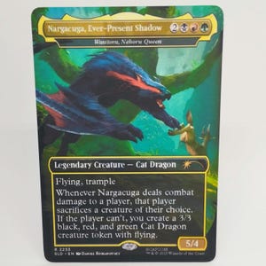 Pode incluir: Carta colecionável com "Nargacuga, Ever-Present Shadow". A carta tem uma borda verde e dourada com uma ilustração de um dragão-gato preto e azul. O texto da carta inclui "Voar, atropelar" e instruções do jogo. A carta é 5/4.