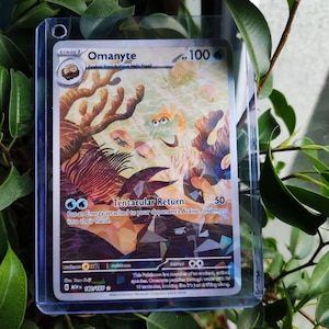 Puede incluir: Una carta holográfica de Pokémon Omanyte, etapa 1, con 100 PS. La carta presenta una escena submarina con corales y criaturas marinas. El texto "Tentacular Return" y otros detalles del juego son visibles.
