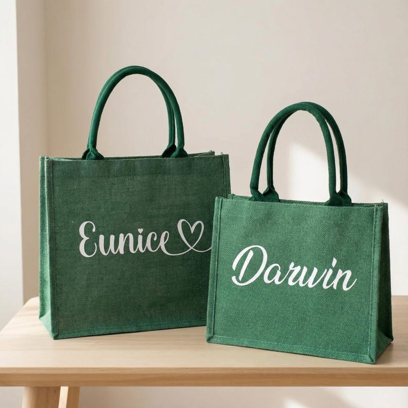 May include: Two green burlap tote bags with matching green handles. The larger bag has the name "Eunice" in white script with a heart symbol. The smaller bag has the name "Darwin" in white script.