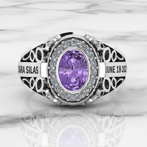 May include: A silver ring with an oval, purple gemstone at the center, surrounded by small, clear stones. The ring has the engraved text "ARA SILAS" and "JUNE 18 2020" on the sides. The ring is displayed on a reflective surface.