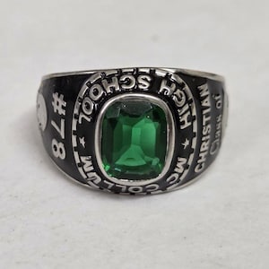 May include: Silver-tone class ring with a large, emerald-green rectangular stone at the center. The black band features the text "MC CHRISTIAN HIGH SCHOOL" and "Class of 78".